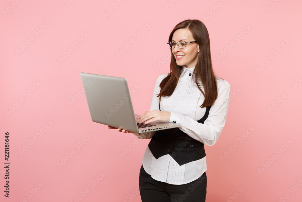Young pleasant successful attractive business woman in glasses holding using laptop pc computer isolated on pink background. Lady boss. Achievement career wealth concept. Copy space for advertisement. Young pleasant successful attractive business woman in glasses holding using laptop pc computer isolated on pink background. Lady boss. Achievement career wealth concept. Copy space for advertisement.