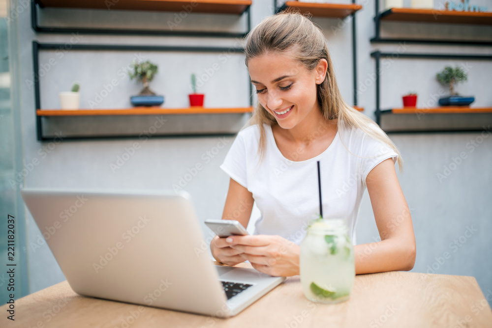 Young woman drinking lemonade and surfing the web. Using phone and laptop.