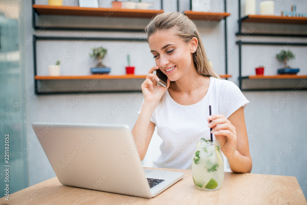 Girl talking on the phone and drinking lemonade while looking at laptop.