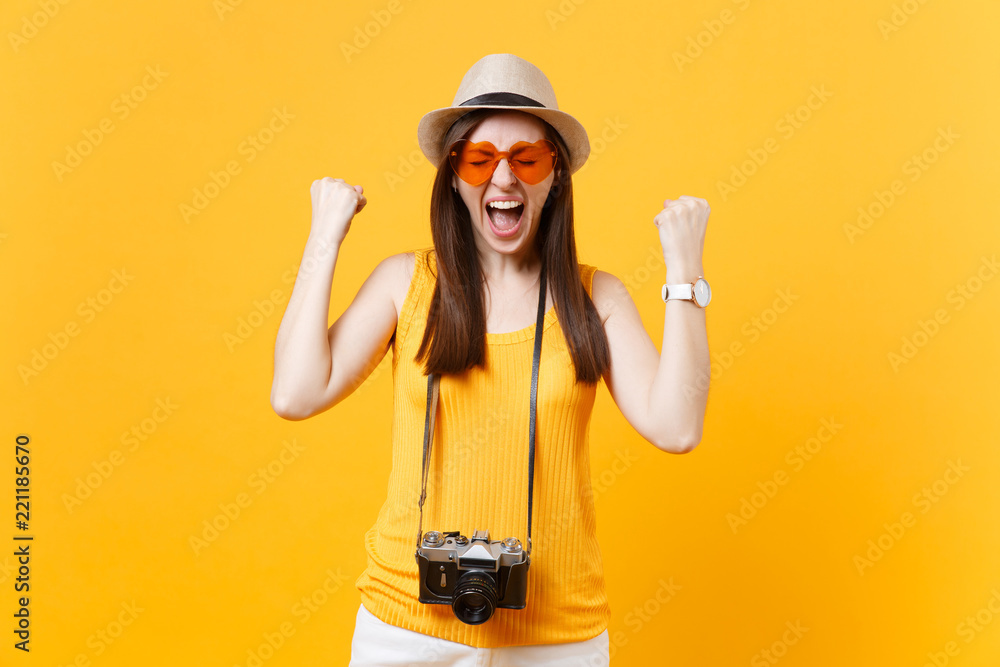 Fun tourist woman in summer casual clothes hat with photo camera clenching fists like winner isolated on yellow background. Girl traveling abroad travel on weekends getaway. Air flight journey concept