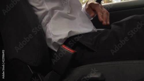 An Unknown Businessman In A White Shirt And Black Pants Sits At The Wheel Of His Car And Fastens A Seat Belt