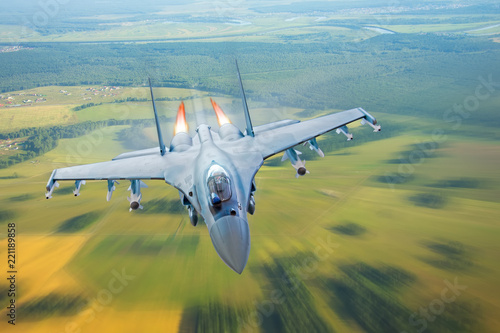 Obraz na plátně Combat fighter jet on a military mission with weapons - rockets, bombs, weapons on wings, at high speed with fire afterburner engine nozzles, flies over the terrain
