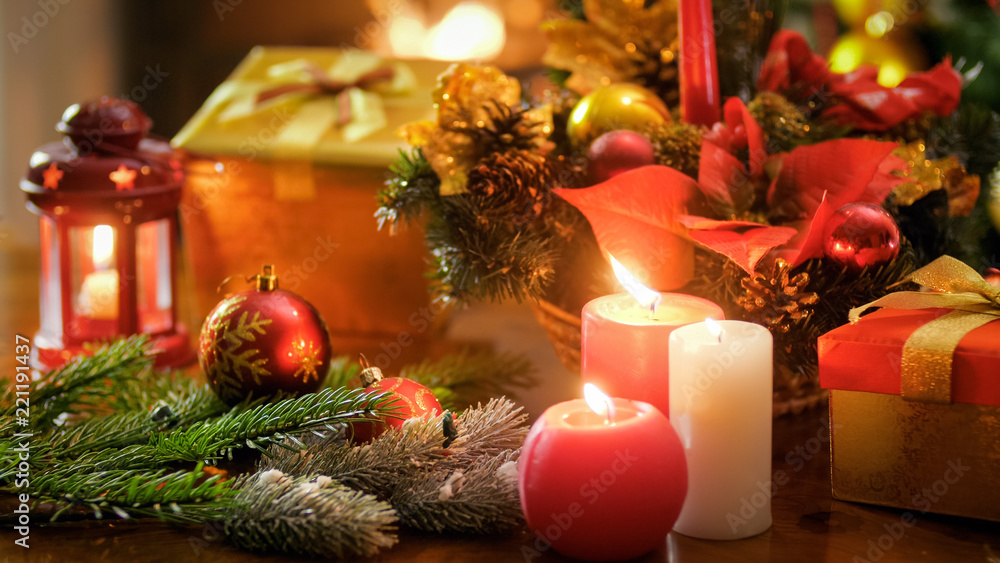 Closeup image of burning candles against Christmas decorations and gift boxes