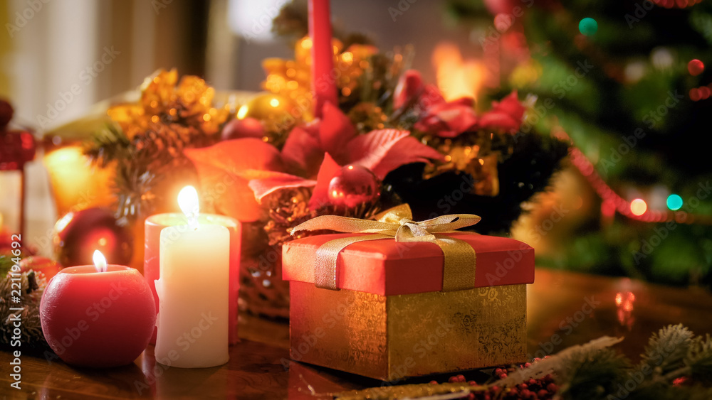 Closeup image of burning candles standing against gift box and Christmas tree Closeup image of burning candles standing against gift box and Christmas tree