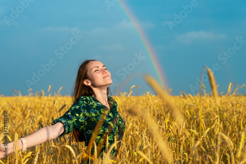 Portrait of a young woman in a wheat field with her arms outstretched inhales clean air on a rainbow background