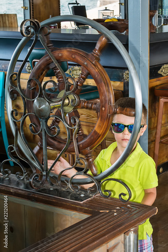 Little boy captain with steering wheel on ship