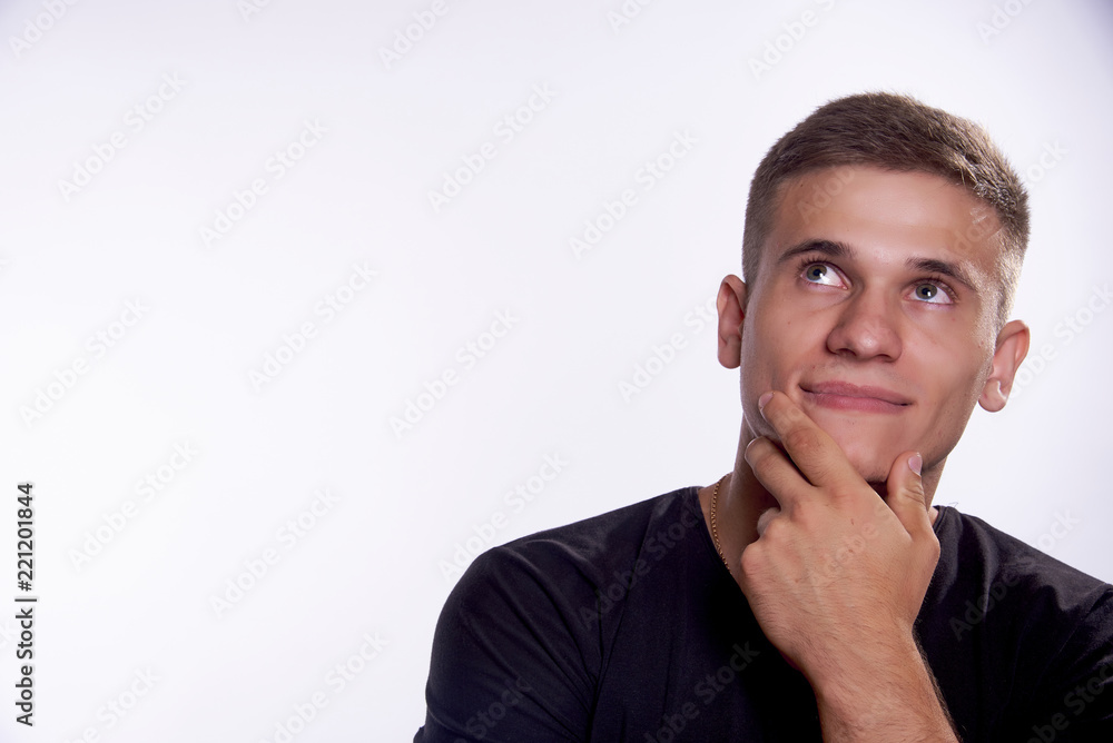 A young man in a black T-shirt laid his hand on his chin and looked thoughtfully upwards A young man in a black T-shirt laid his hand on his chin and looked thoughtfully upwards
