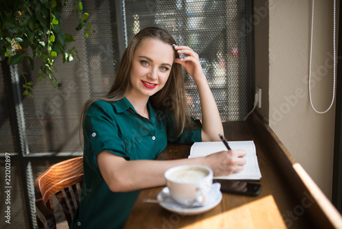 Young beautiful girl sitting in a cafe and drinking coffee and writing in a notebook