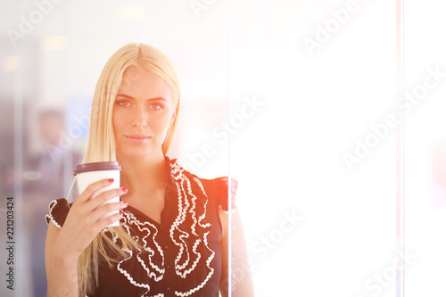 Businesswoman holding a cup of coffee standing in office .