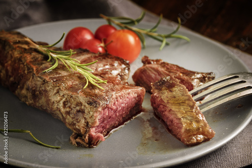 Grilled rump steak with rosemary garnish and tomatoes on a gray plate, rustic style