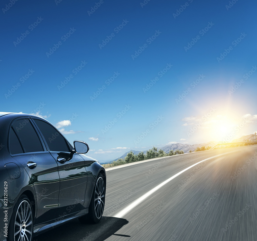 Naklejka premium Czarny samochód pędzący w słońcu szybką autostradą.