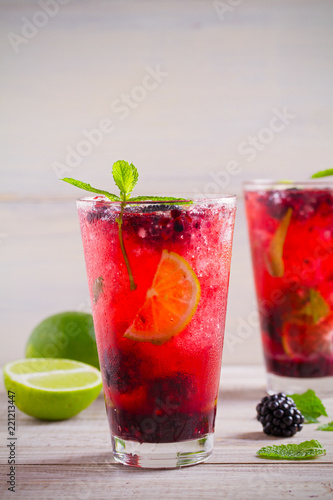 Blackberry mojito cocktail with berries, lime and mint on wooden background. vertical