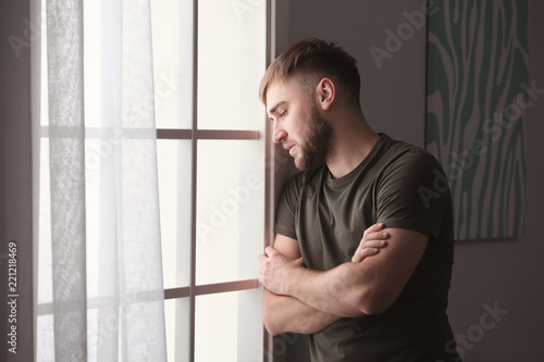 Depressed young man near window at home