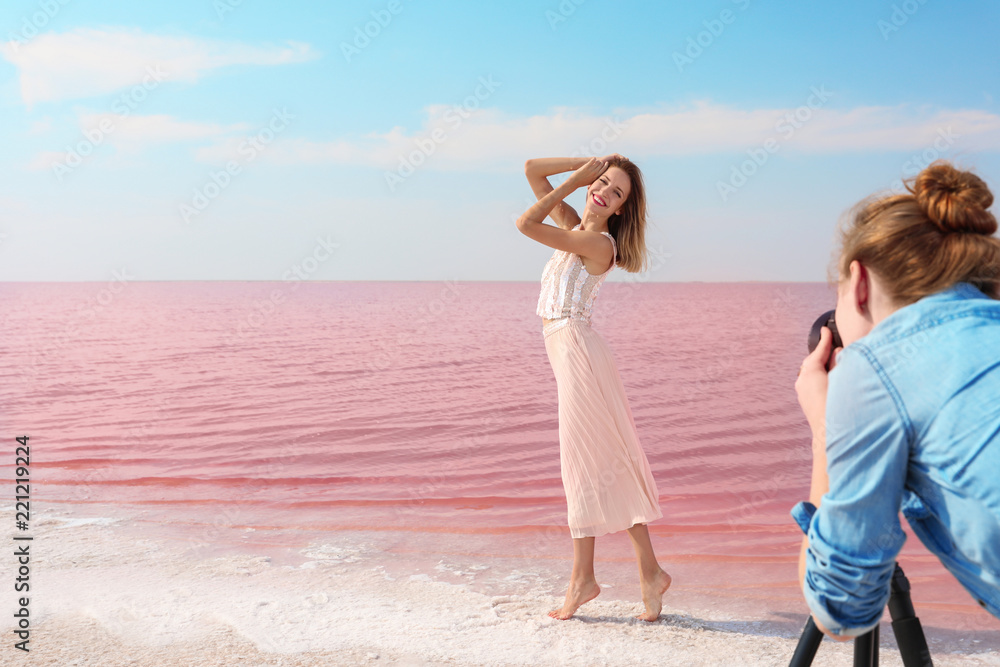 Female photographer taking pictures of model near pink lake