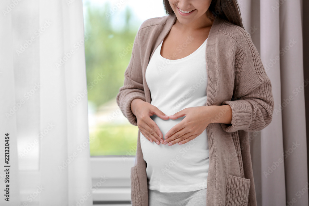 Pregnant woman standing near window at home, closeup Pregnant woman standing near window at home, closeup
