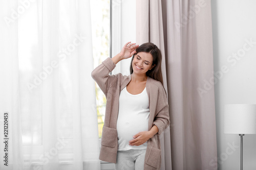 Happy pregnant woman standing near window at home