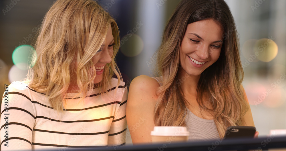 Two lovely girls with smart phone at night in downtown cafe Two lovely girls with smart phone at night in downtown cafe