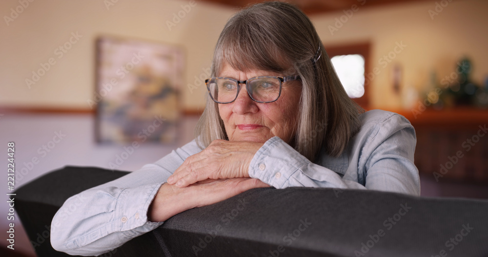 Obraz premium Pensive senior lady resting head on hands and thinking to herself in living room