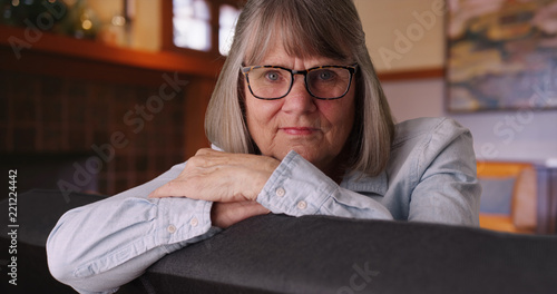 Φωτογραφία Somber thoughtful old white lady looking at camera sitting on living room couch