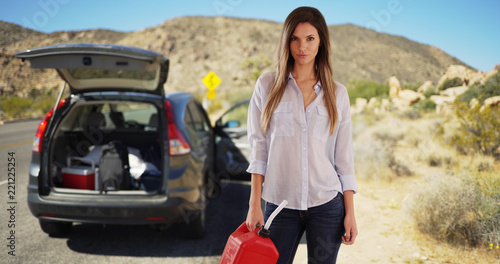 White woman holding gasoline container after running out of gas in the desert