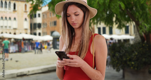 Caucasian hipster girl in her 20s texting on cellphone in Italian city setting