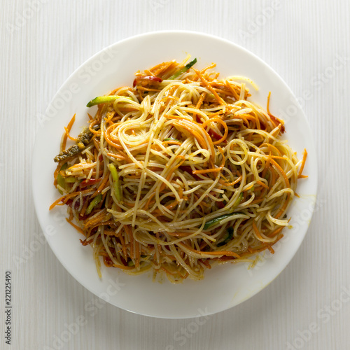 Rice noodles Funchoza with vegetables in a white plate. Traditional Korean cuisine