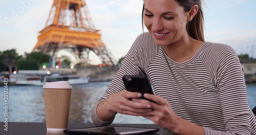 Photography Caucasian woman with coffee messaging on smartphone sitting by Eiffel Tower