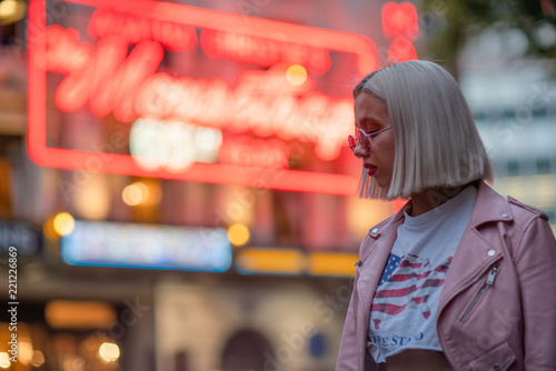 Blond girl in fashionable sunglasses and leather jacket with neon lights