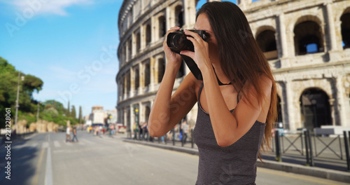 Young tourist woman standing near the Roman Coliseum taking picture with camera