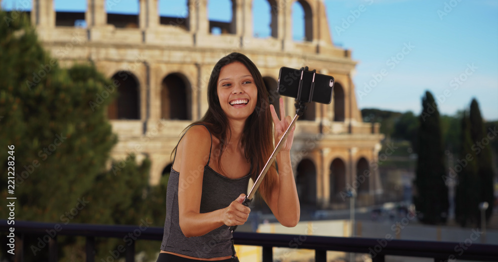Cute brunette traveler girl in front of the Roman Coliseum using selfie stick