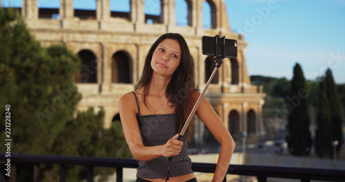 Cute brunette traveler girl in front of the Roman Coliseum using selfie stick
