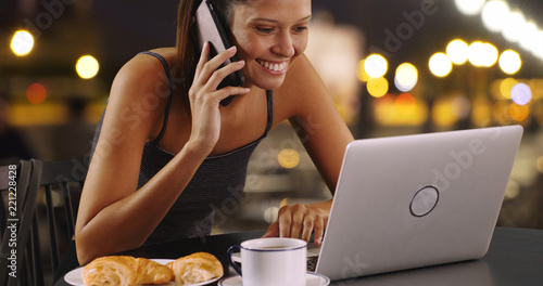Young woman talking on mobile phone and working on laptop outside at night