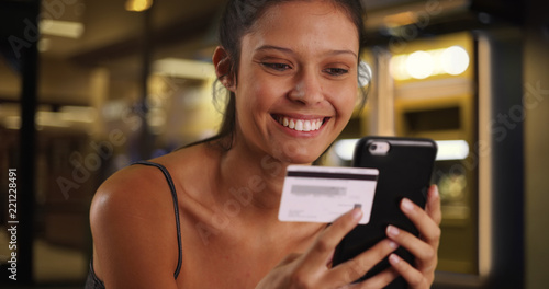 Young brunette female standing on street at night online shopping with phone