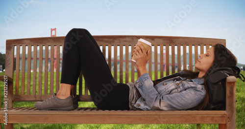 Hipster girl in jean jacket lies on park bench near Golden Gate bridge wondering