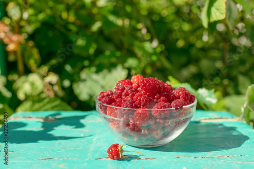 Ripe fresh raspberries in a glass bowl on a wooden table.