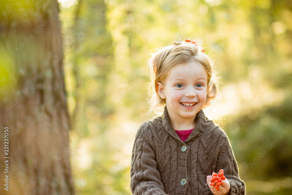 Cute toddler girl wearing knitted sweater,holding rowanberry. fall, red and yellow leaves.cute child girl playing rowan berry beads in sunny autumn garden.She holds an orange rowan in her hands.Copy Cute toddler girl wearing knitted sweater,holding rowanberry. fall, red and yellow leaves.cute child girl playing rowan berry beads in sunny autumn garden.She holds an orange rowan in her hands.Copy