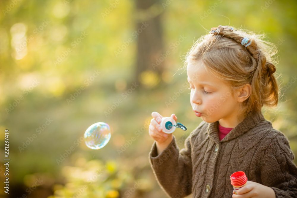 Five years old caucasian child girl blowing soap bubbles outdoor at sunset - happy carefree childhood.Fall seasom, bright colors, happy childhood. Walking in autumnal park.Copy space