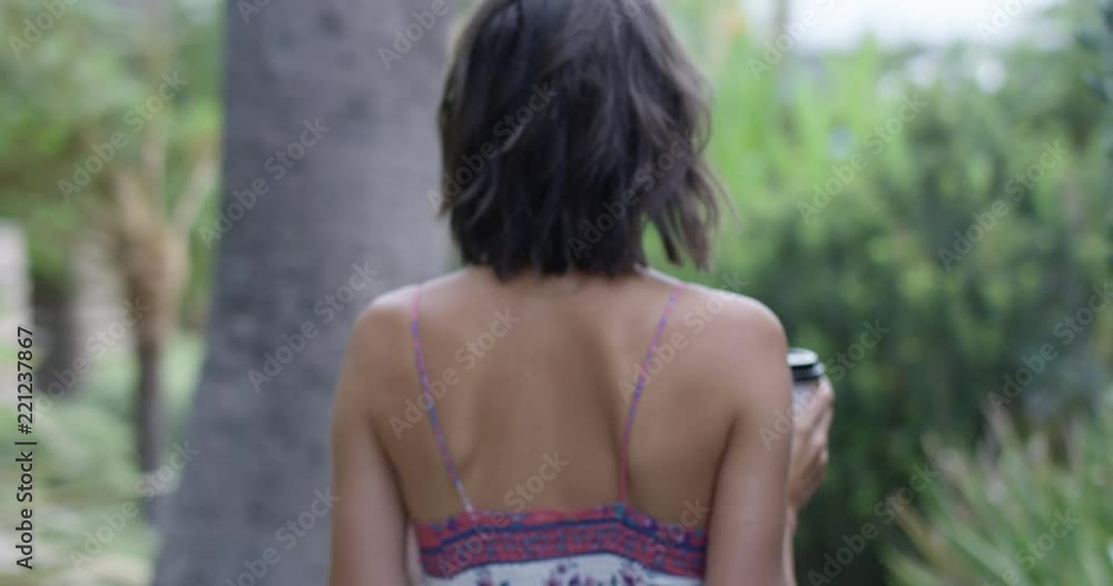 Woman walking through park area with two coffee cups Woman walking through park area with two coffee cups