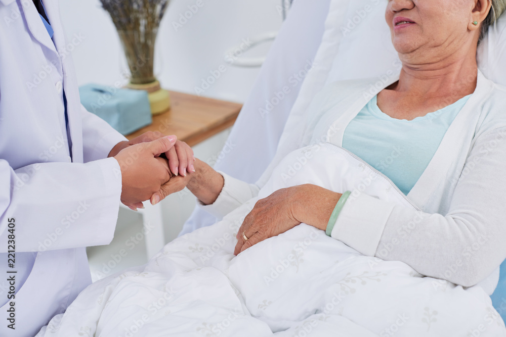 Female doctor holding hand of senior patient to support her Female doctor holding hand of senior patient to support her