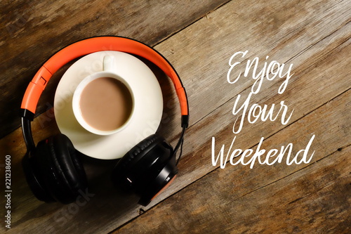 Top view of headphones and a cup of coffee on wooden background written with ENJOY YOUR WEEKEND photo