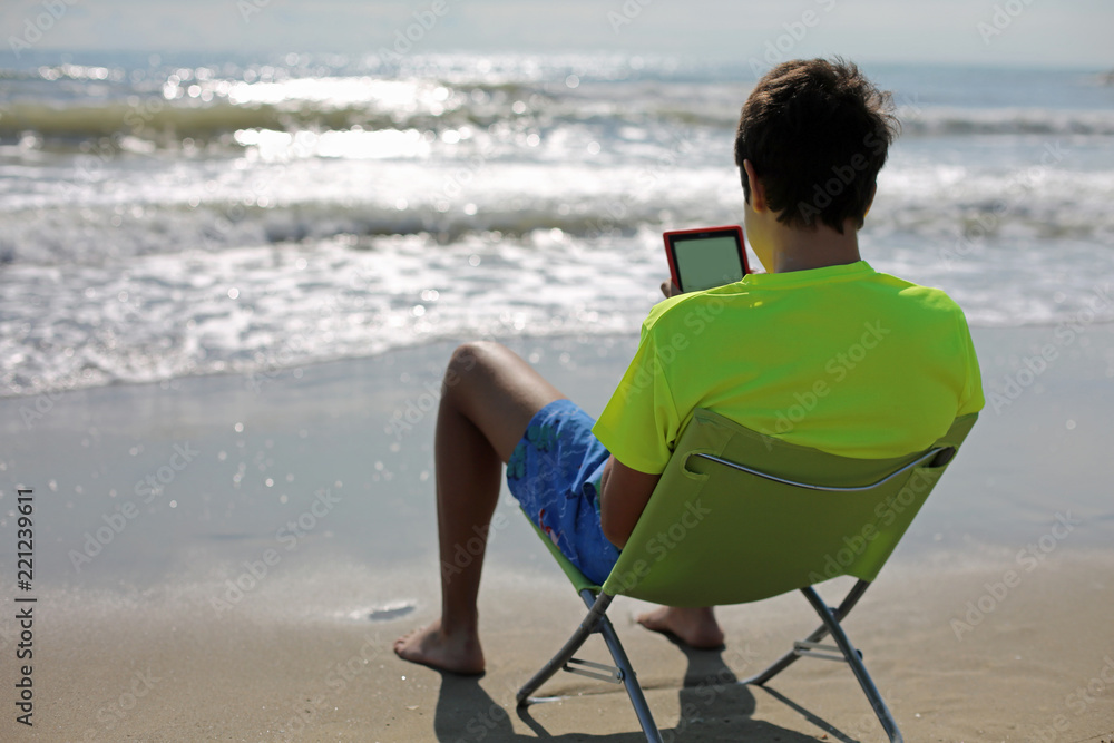 boy reads a digital book in front of the sea