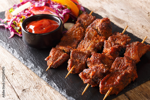 Recipe of a spicy African suya kebab on skewers with fresh vegetable salad and ketchup close-up. horizontal