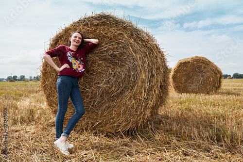 young girl having fun in the field, mowed hay wrapped in a haystack