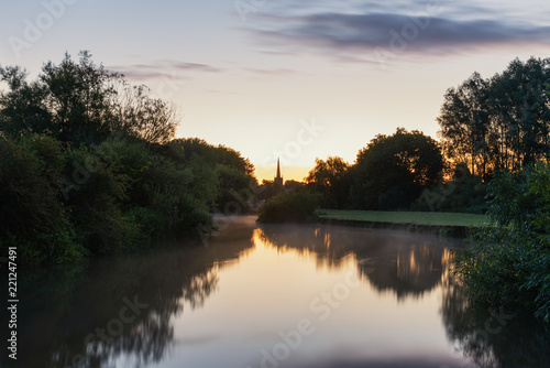 Beautiful dawn landscape image of River Thames at Lechlade-on-Thames in English Cotswolds countryside with church spire in background