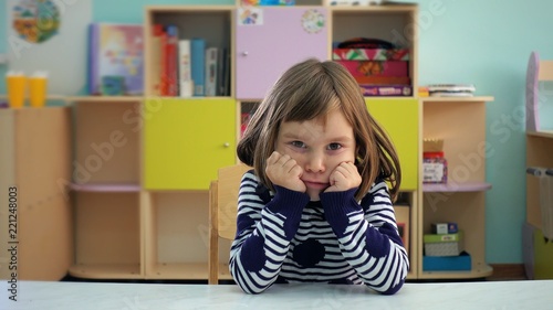 Kindergarten. The child shows different emotions. The girl is 5-6 years old with blond hair. The child is very emotional, shows sadness and joy in the children's playroom.