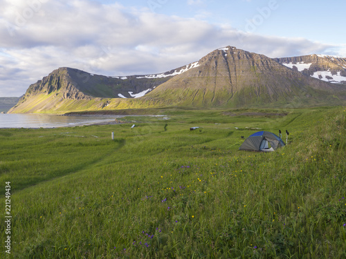 Alone small tent standing at Hloduvik cove campsite with green grass meadow, Skalarkambur mountain, wooden logs and footpath, Hornstrandir, west fjords, Iceland photo