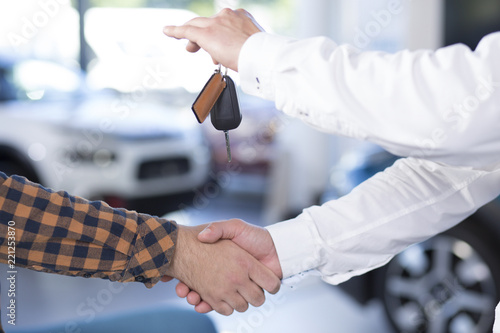 Close-up of two men giving a handshake. Seller holding car keys