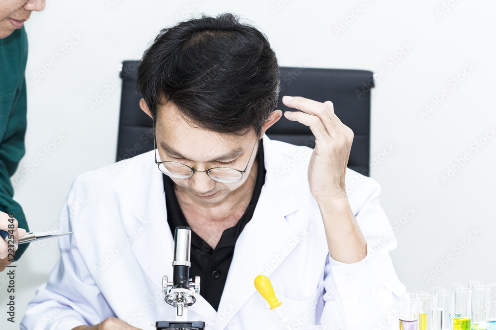 Senior handsome researcher and assistant professor looking with microscopes near color test tube.Doctor in white suit and glasses .Copy space. Senior handsome researcher and assistant professor looking with microscopes near color test tube.Doctor in white suit and glasses .Copy space.