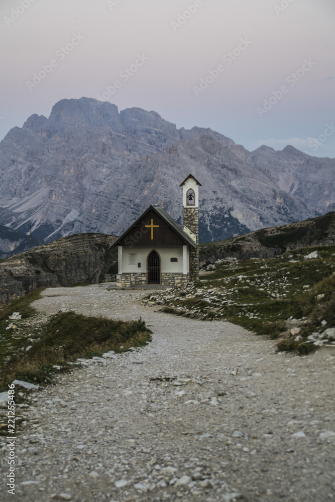 Fototapeta premium Breathtaking summer scenic landscape view of iconic Cappella degli Alpini chapel while sunrise in famous Tre Cime di Lavaredo mountains in the Dolomites mountain range, South Tirol Alps, Italy, Europe