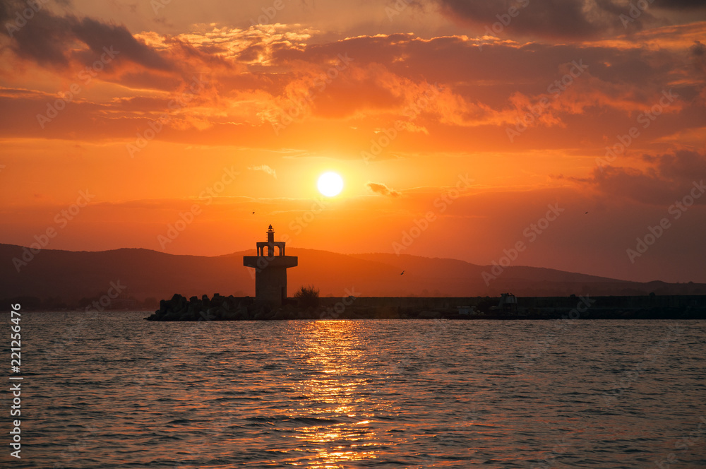 Lighthouse against a beautiful evening sunset on the sea. Amazing sunset on black sea and beautiful cloudscape.